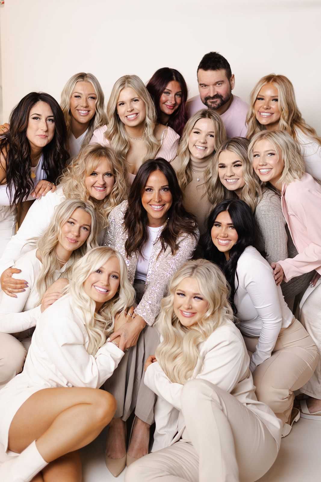 Group of 15 smiling people, mostly women, posing together against a plain background.