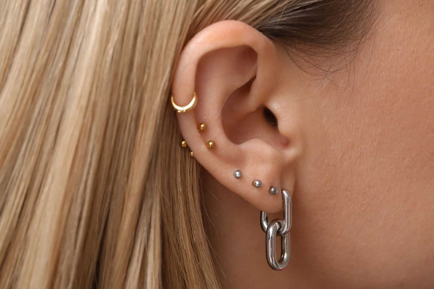 Close-up of an ear with multiple gold and silver piercings, including studs and hoops.